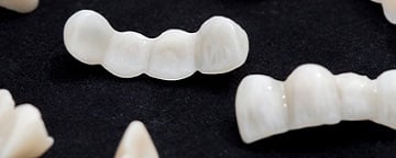 Dental ceramic or zirconium tooth bridges on dark black surface.
